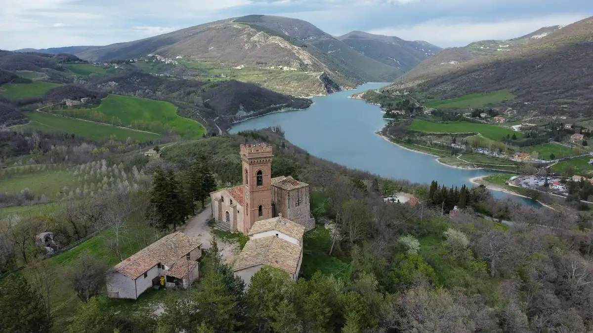 Serene aerial view of historic castle atop verdant hill in Tuscan-Umbrian Corridor, overlooking shimmering lake and lush valley.