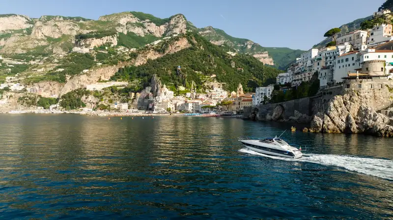 A yacht cruises along the picturesque Amalfi coastline under clear blue skies during summer.