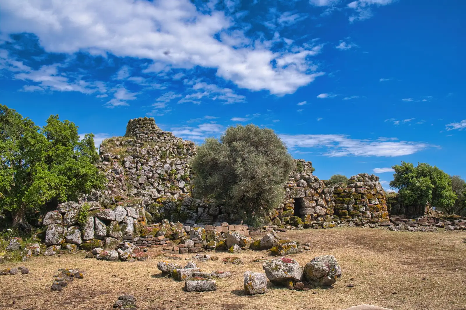 Explore the ancient Nuraghe ruins set against a vibrant blue sky in the Mediterranean landscape.