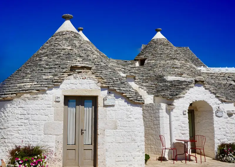 Exterior view of a conical-roofed trullo house under a clear blue sky in Alberobello, Italy.